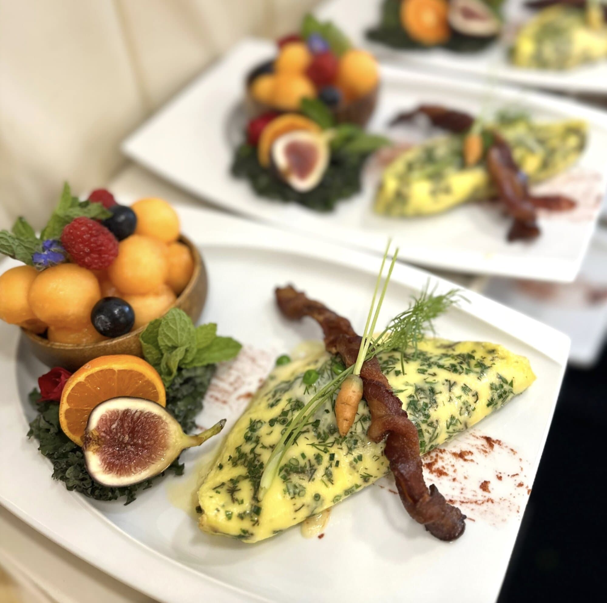 Herbed omelette plated with figs, melon, and crisped bacon